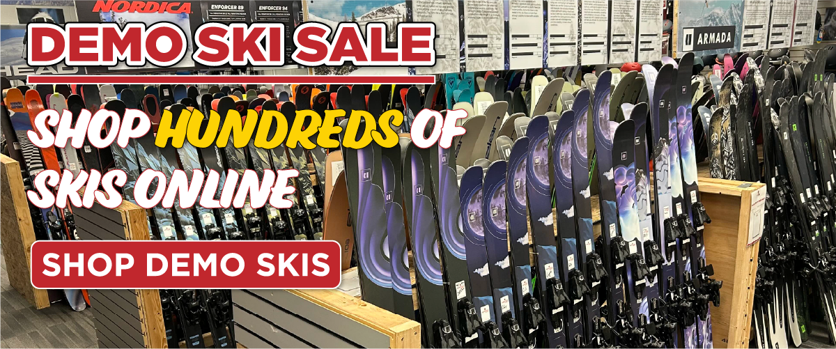 demo_skis_1200x500 Rows of skis lined up in a store display with signs reading Demo Ski Sale, Shop hundreds of skis online, and a button that says Shop Demo Skis. Various ski brands are visible in the background.