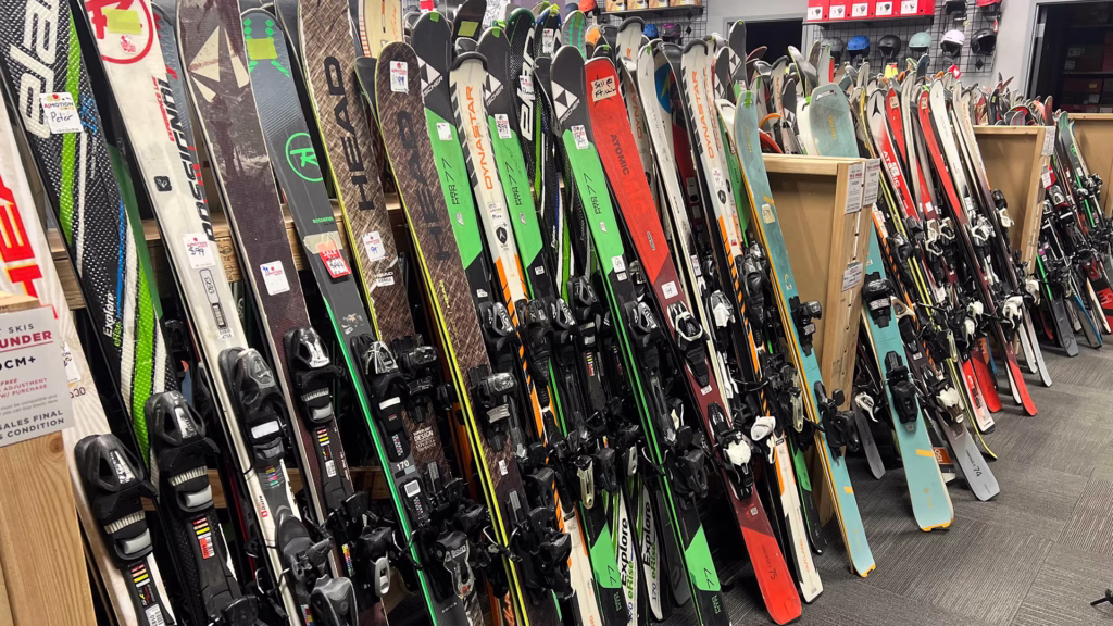 used_rental-skis_1920x1080 A display of various colorful skis standing upright in rows inside a ski shop, with different brands, sizes, and bindings visible on a carpeted floor.
